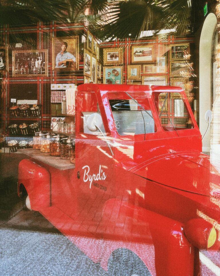 Red vintage car reflected in shop window with jars and decor in Savannah, GA.